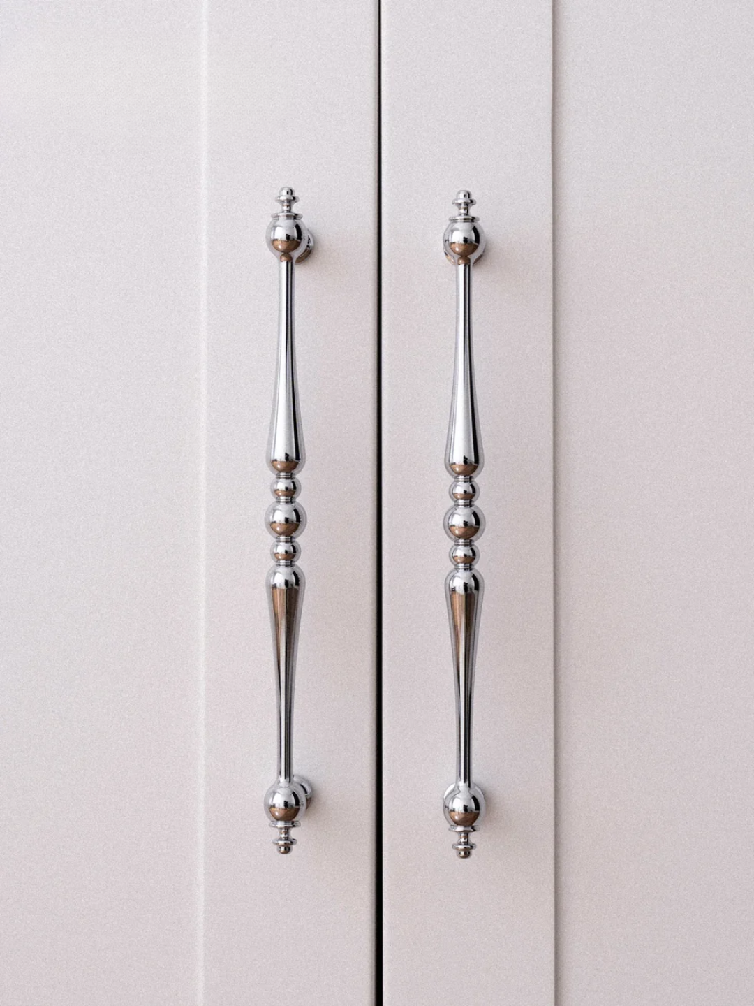 Close-up of two silver cabinet handles on a light gray cabinet.