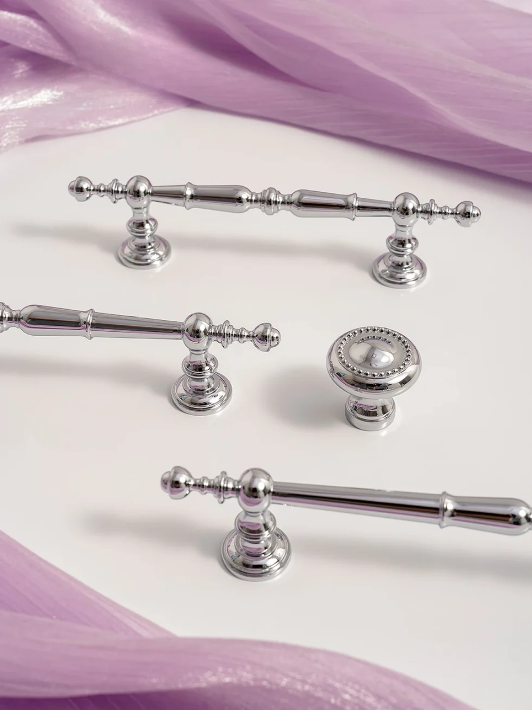 Set of silver cabinet handles and knobs on a white surface with purple fabric in the background