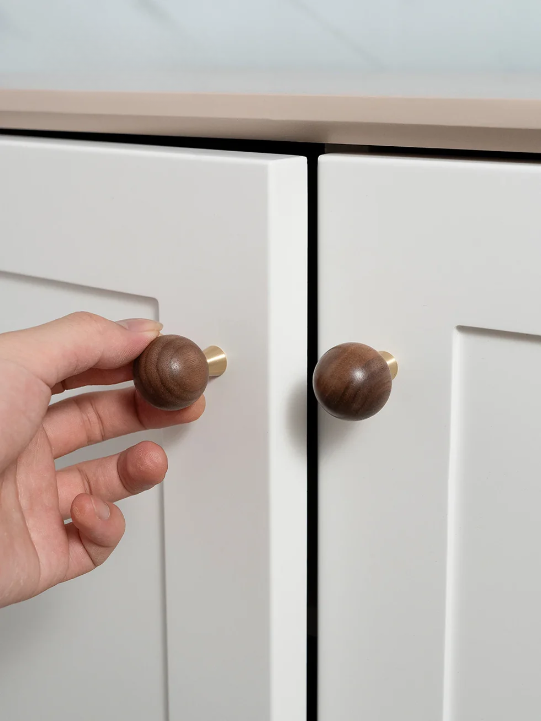 Hand holding a wooden cabinet knob next to a white cabinet with a similar knob.