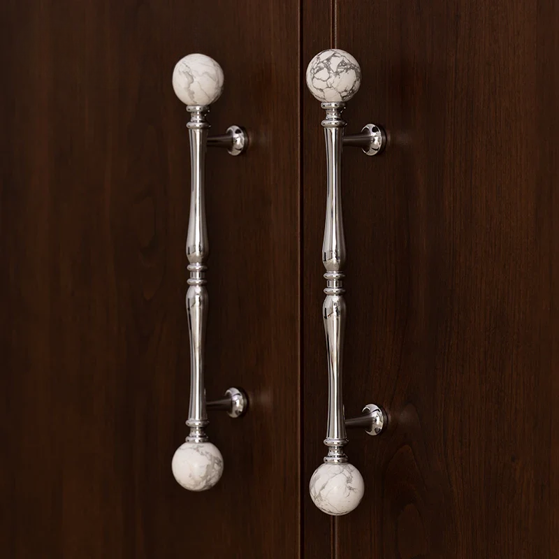 Pair of silver cabinet handles with marble knobs on a wooden door.