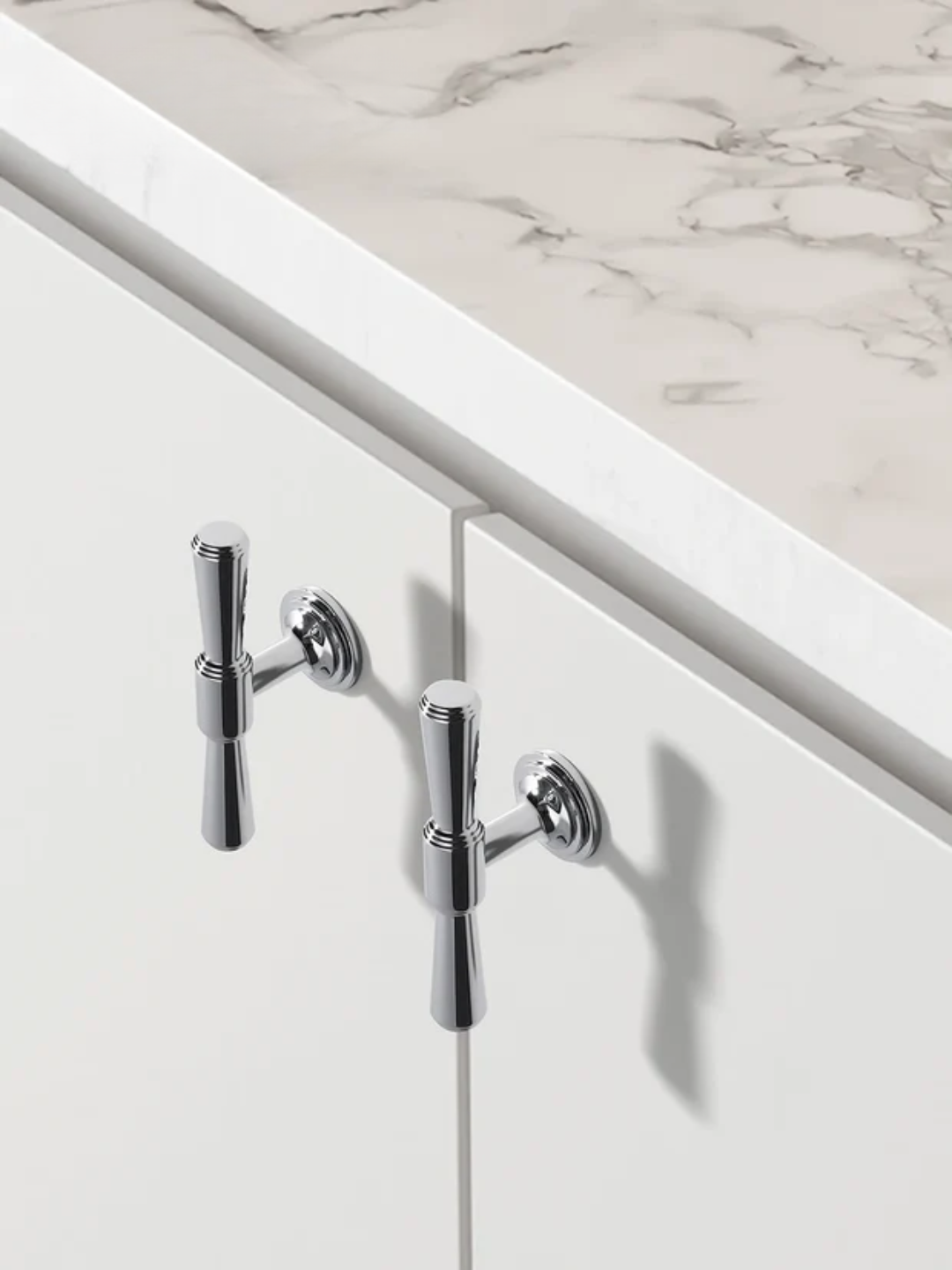 Chrome cabinet handles on a white cabinet with a marble countertop.