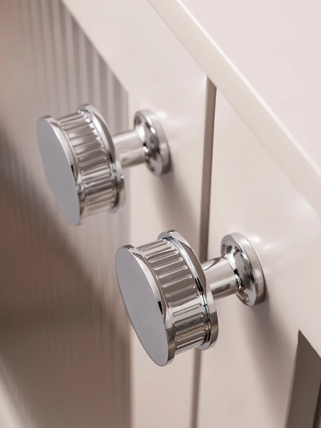 Close-up of silver cabinet knobs on a white wooden cabinet.