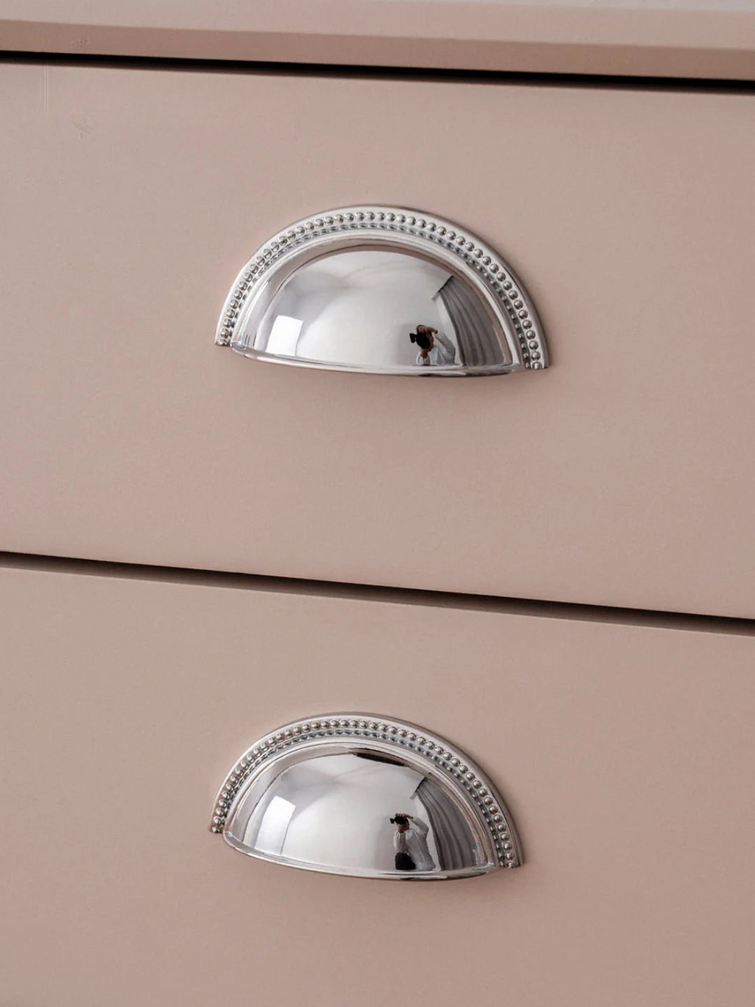 Close-up of two silver cabinet handles on a beige drawer.