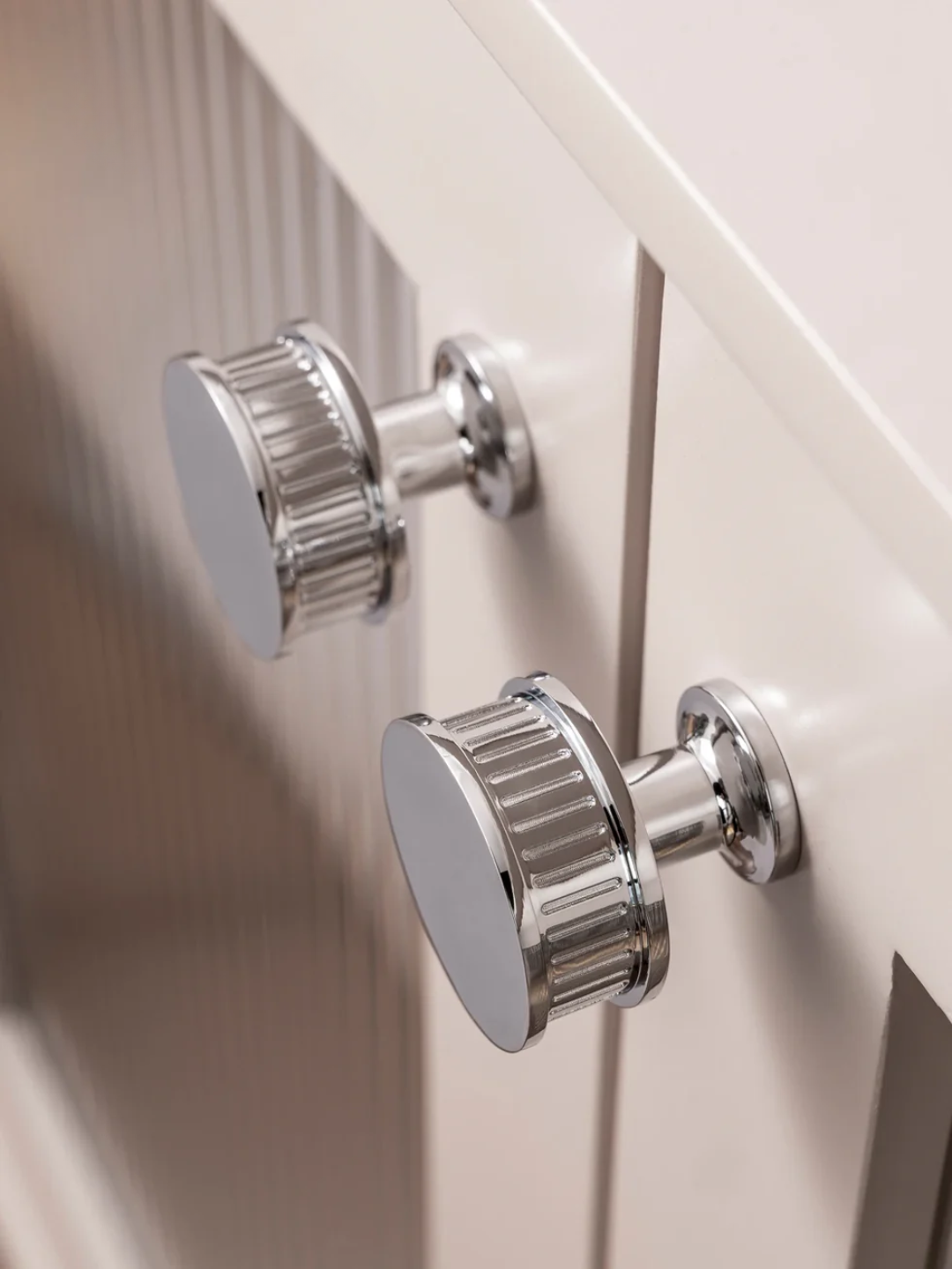 Close-up of two silver cabinet knobs on a white cabinet.