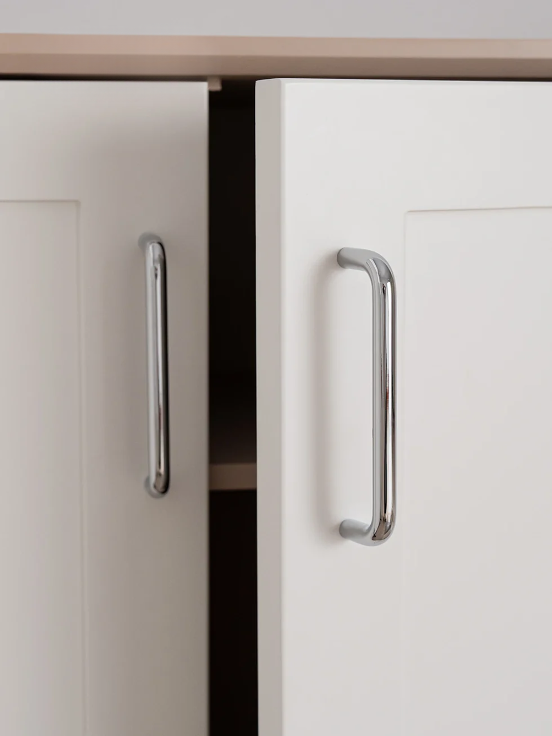 Close-up of a kitchen cabinet with metallic handles on a neutral background