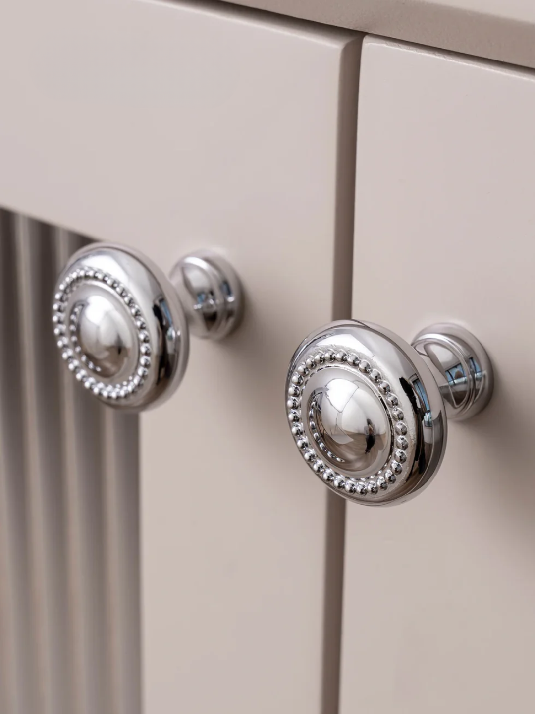 Close-up of a cabinet with decorative silver knobs on a beige background