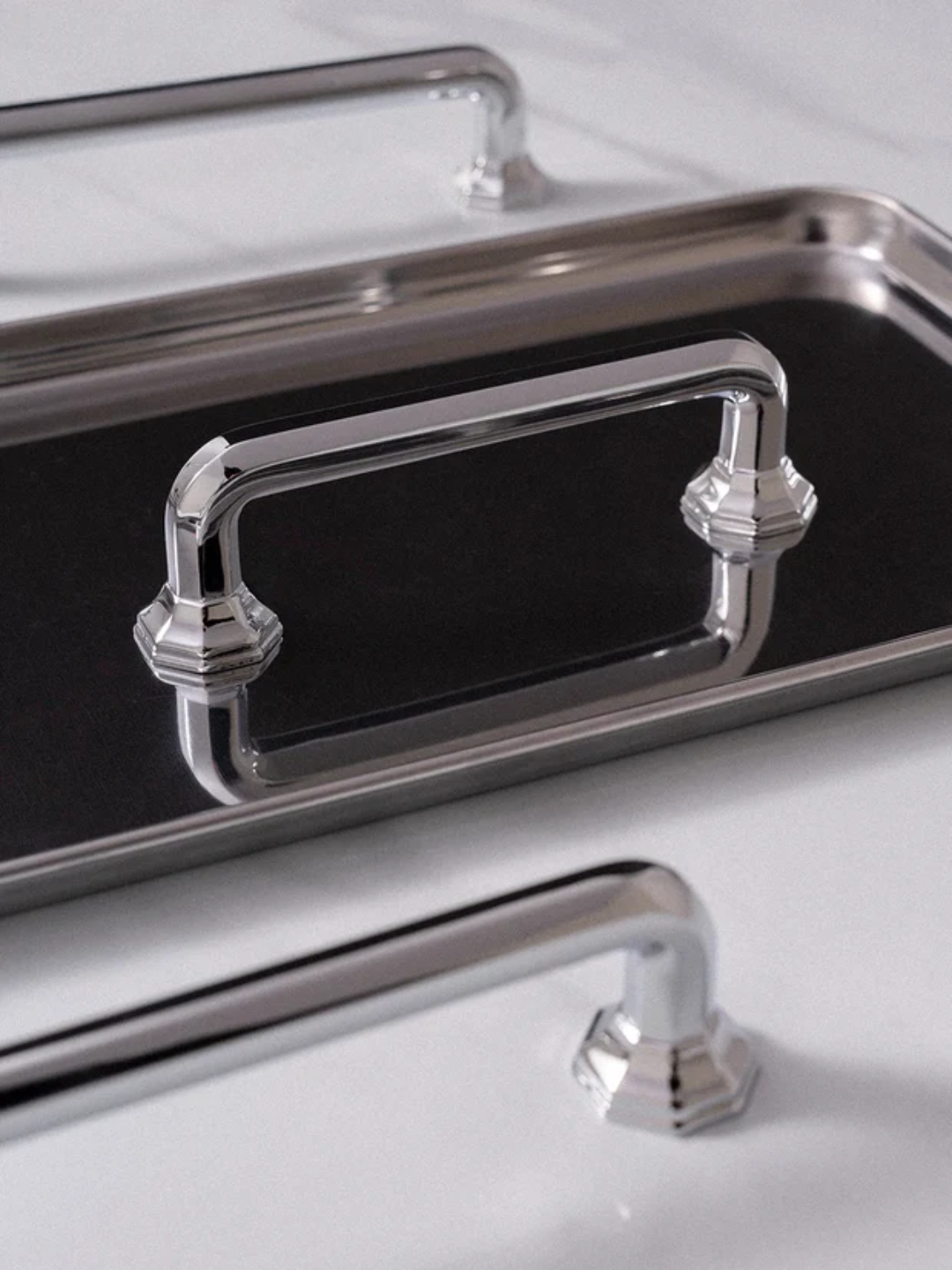 Metallic tray with decorative handles on a reflective surface