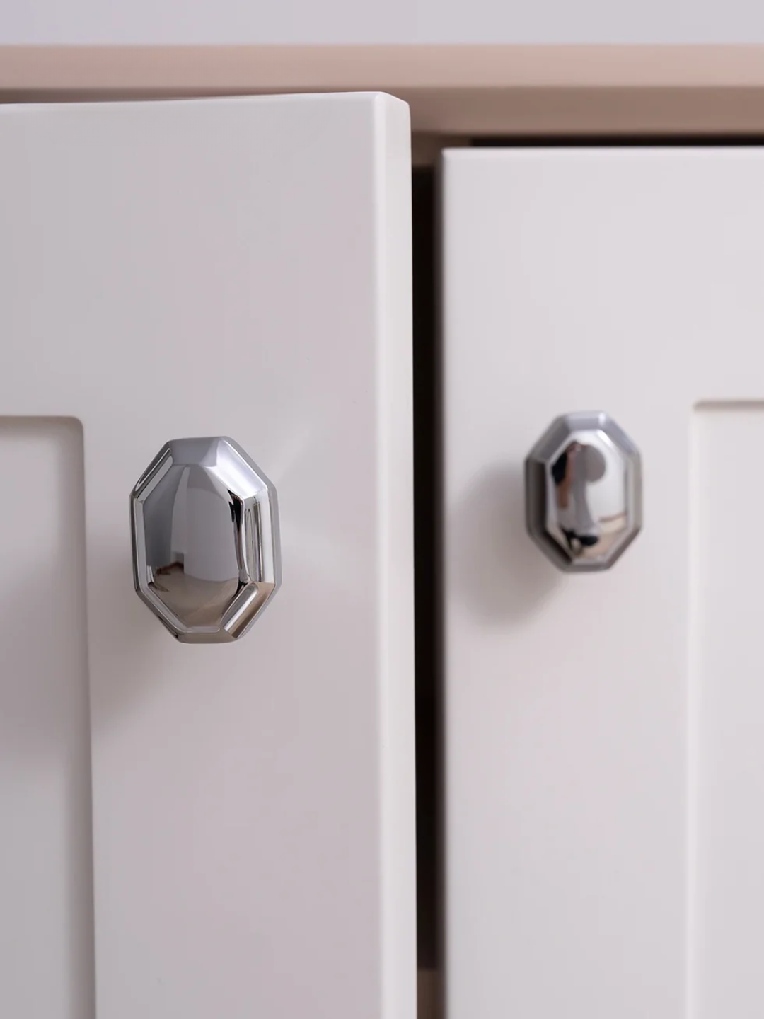 Close-up of two silver cabinet knobs on a light-colored cabinet.