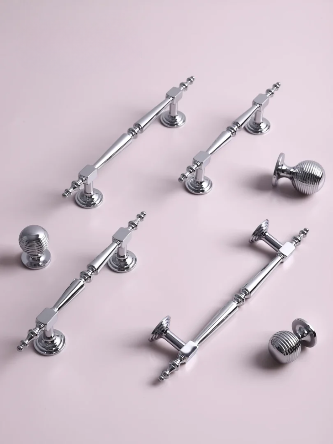 Collection of silver cabinet handles and knobs on a pink background
