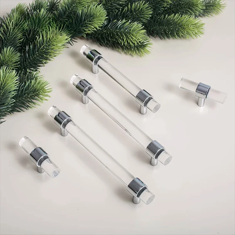 Clear acrylic cabinet handles with silver accents on a light surface with greenery.