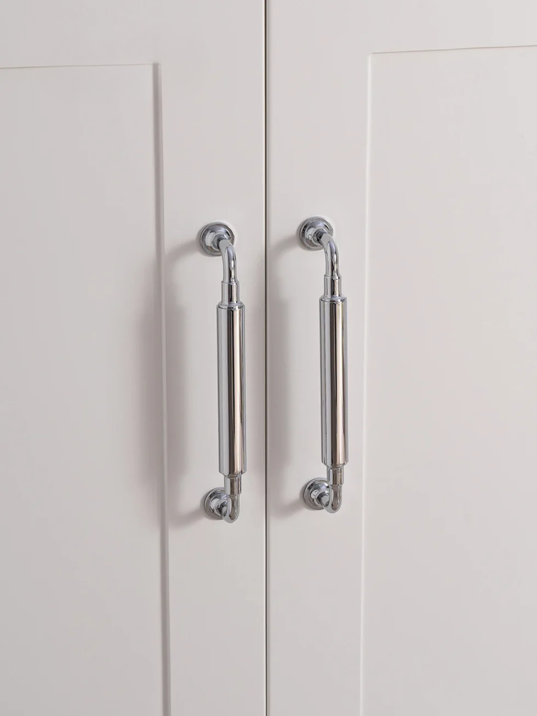 Close-up of a pair of silver cabinet handles on a white door.