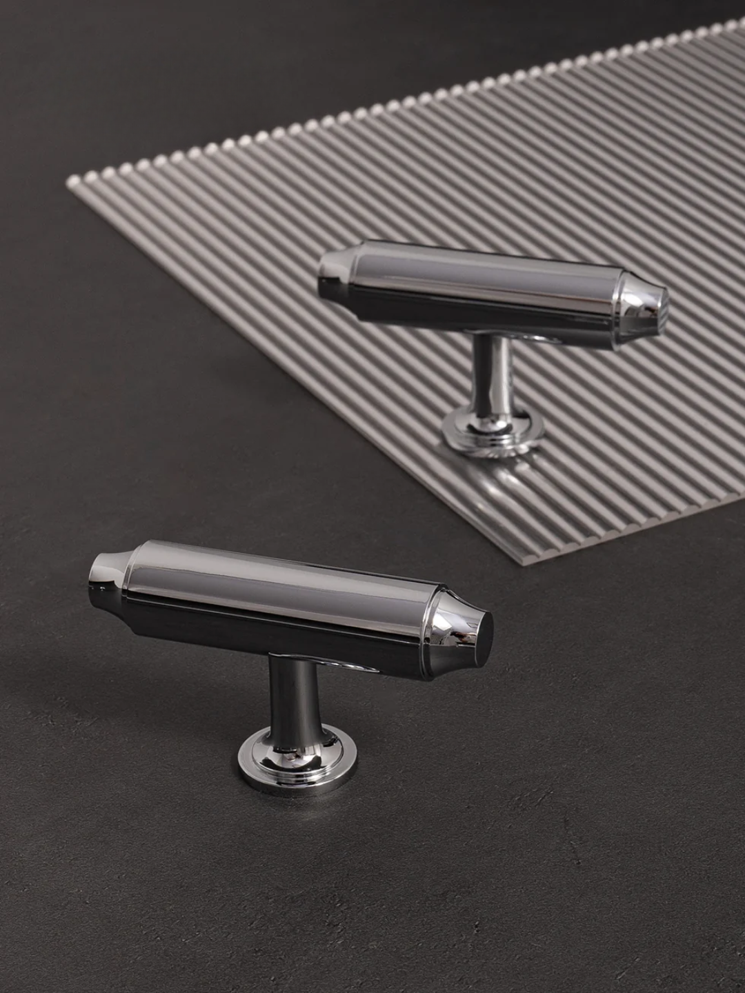 Two metallic t-bar handles on a dark surface with a textured gray mat in the background.