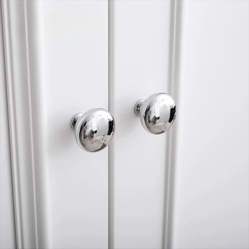 Close-up of two silver cabinet knobs on a white cabinet.