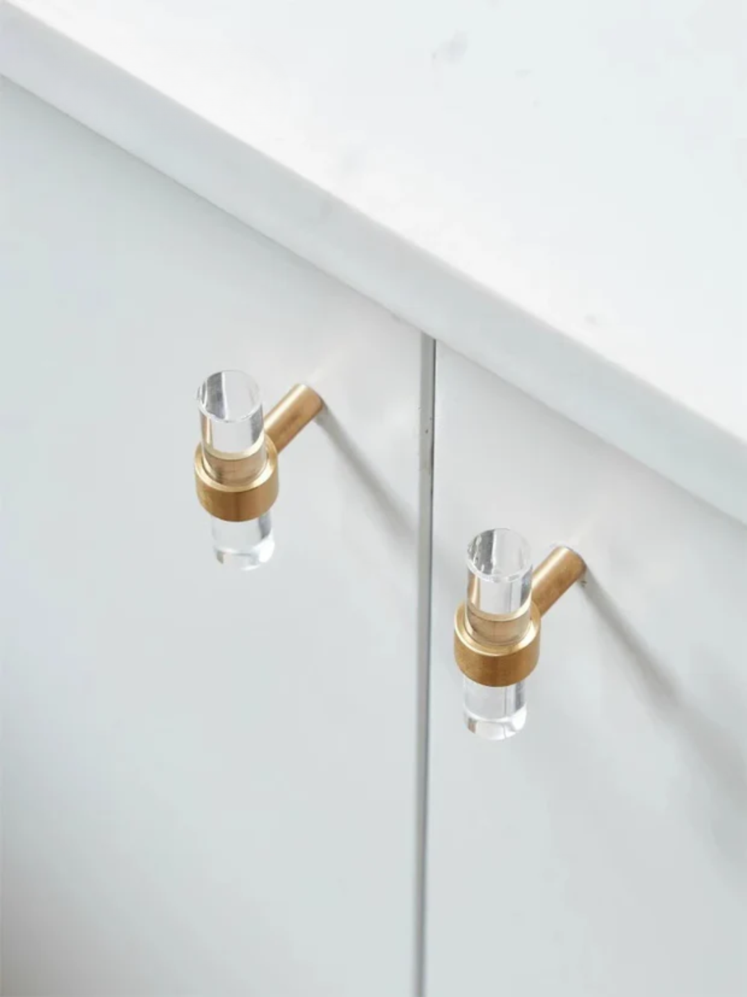 Gold and clear glass cabinet handles on a white cabinet.