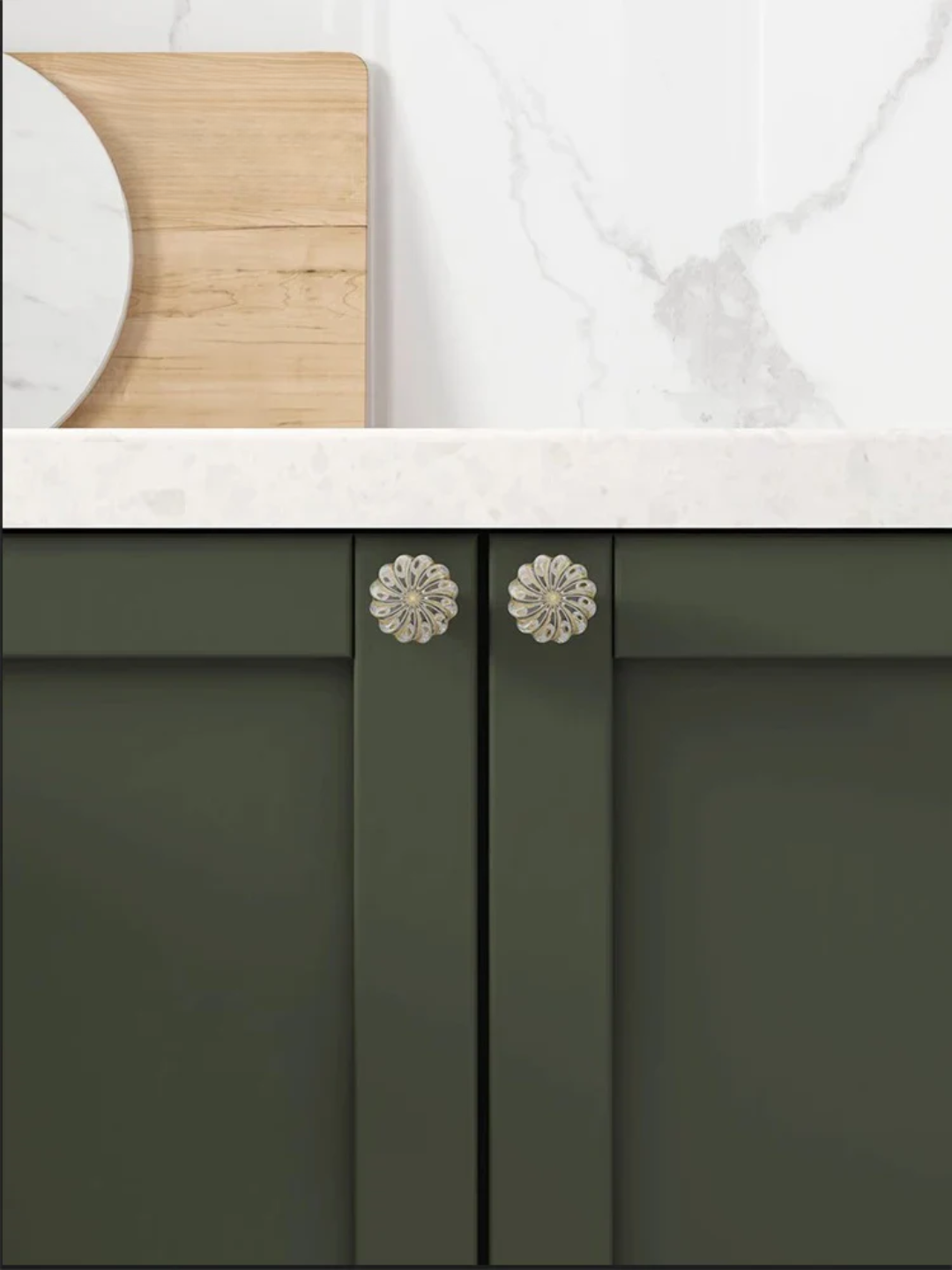 Green kitchen cabinets with decorative knobs on a white countertop.