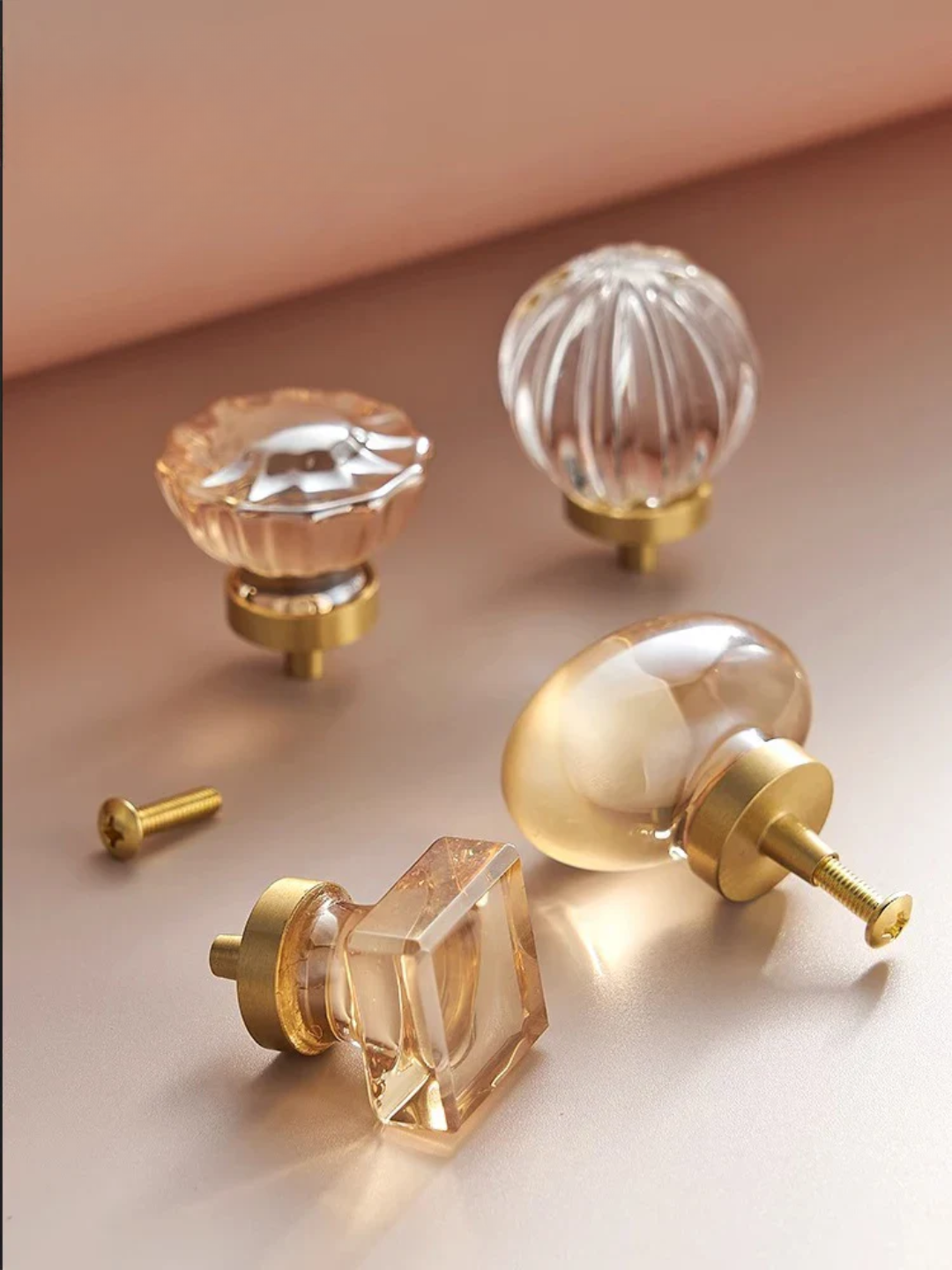 Clear glass cabinet knobs with gold bases on a beige surface