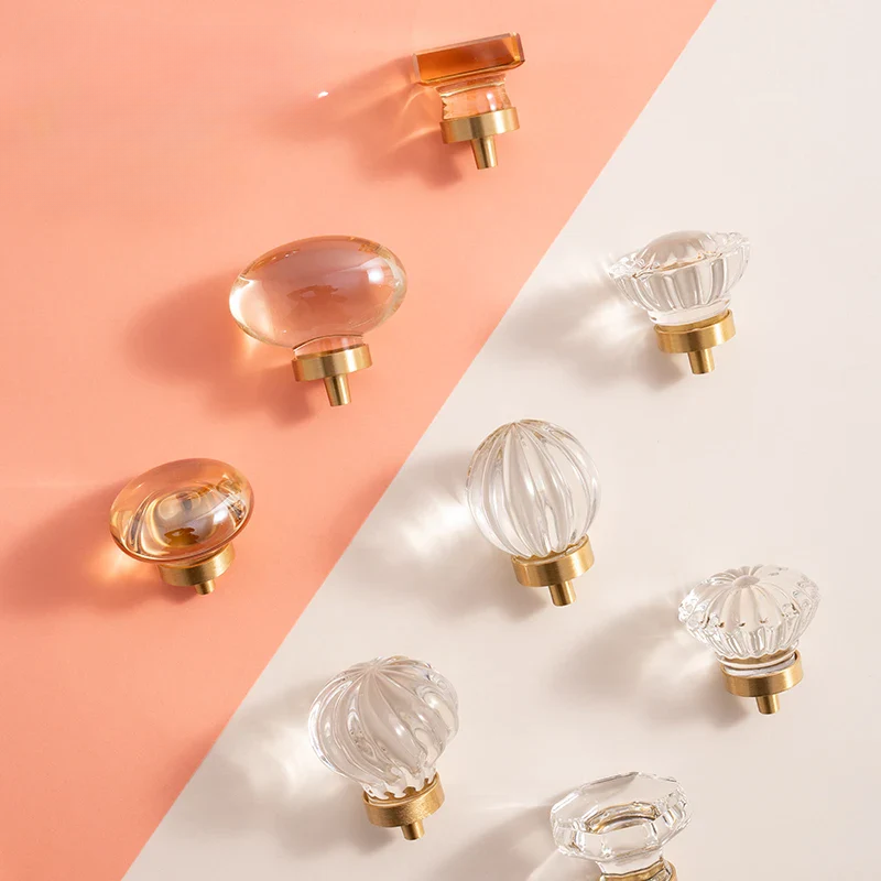 Clear glass cabinet knobs with gold bases on a two-tone pink and white background