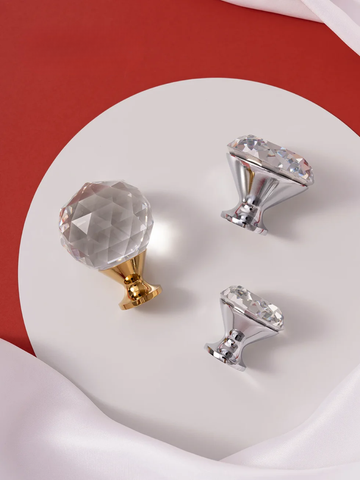 Three crystal knobs in gold, silver, and clear on a white heart-shaped platform with a red background.