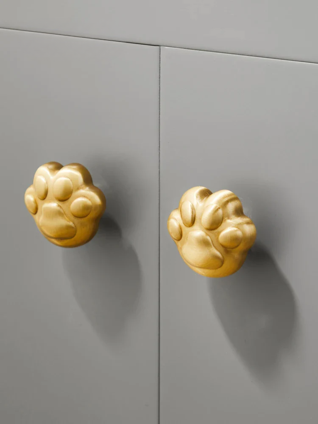 Gold paw-shaped cabinet knobs on a gray cabinet.