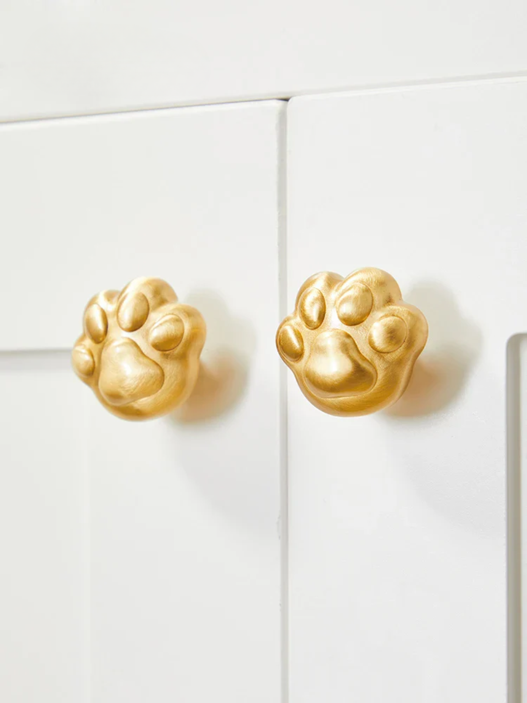 Gold paw-shaped knobs on a white cabinet door