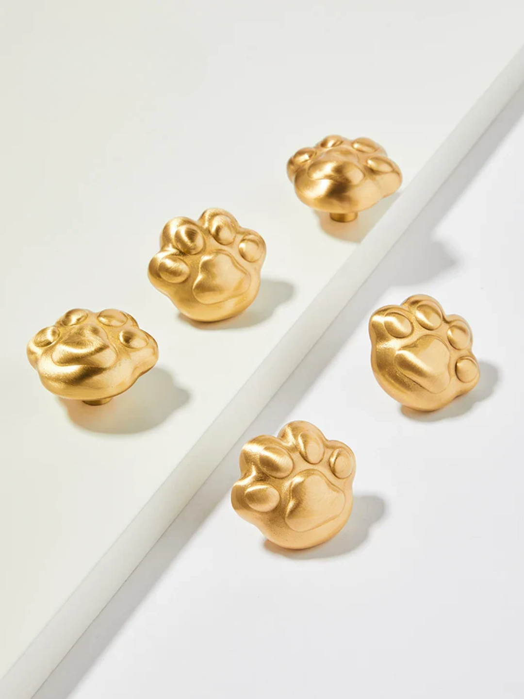 Gold paw-shaped earrings on a light gray background