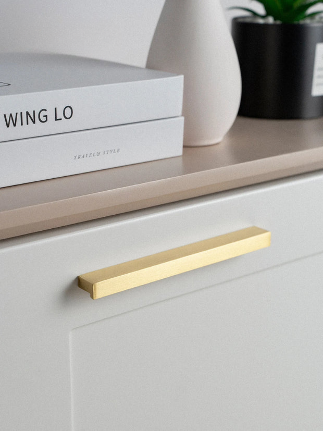 Gold cabinet handle on a white drawer with books and decor items in the background.