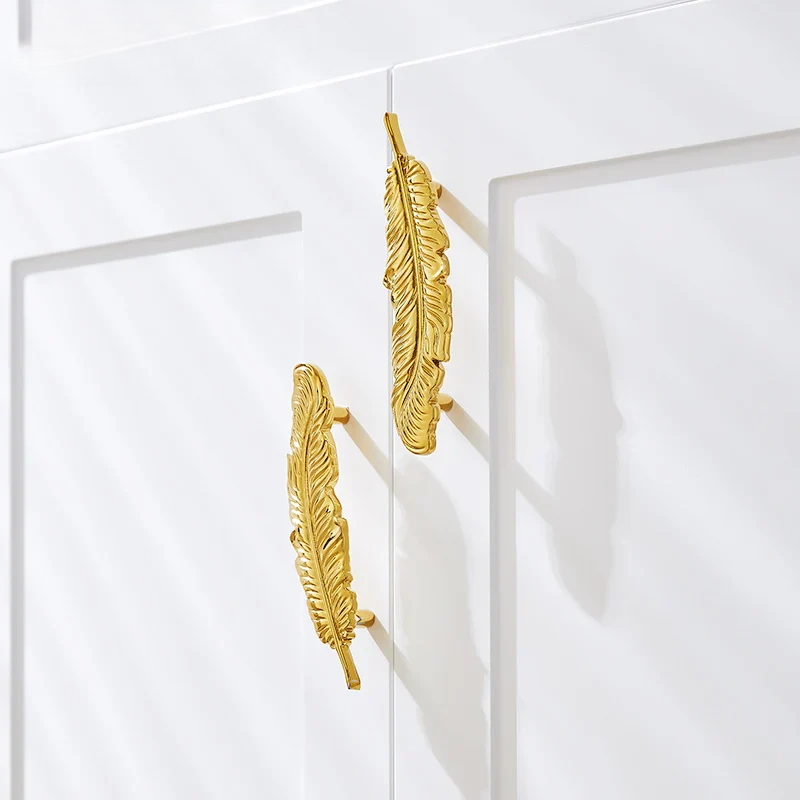 Gold feather-shaped earrings on a white background
