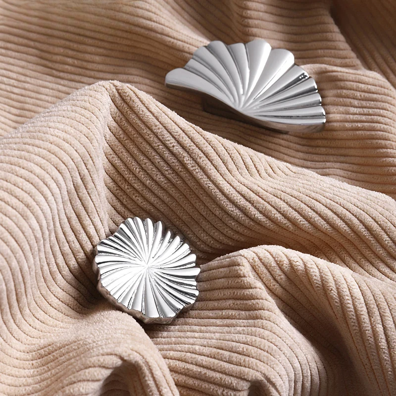 Two silver shell-shaped objects on a textured beige fabric surface