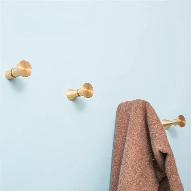 Three gold wall hooks with a brown towel on a light blue background