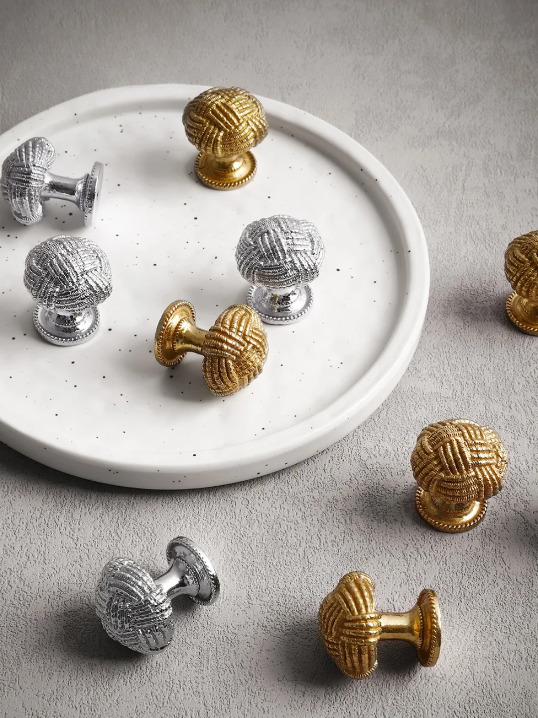 Decorative cabinet knobs in gold and silver on a white plate and gray surface.