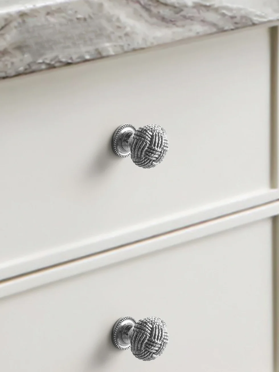 Close-up of a white cabinet with decorative silver knobs on a marble countertop background.