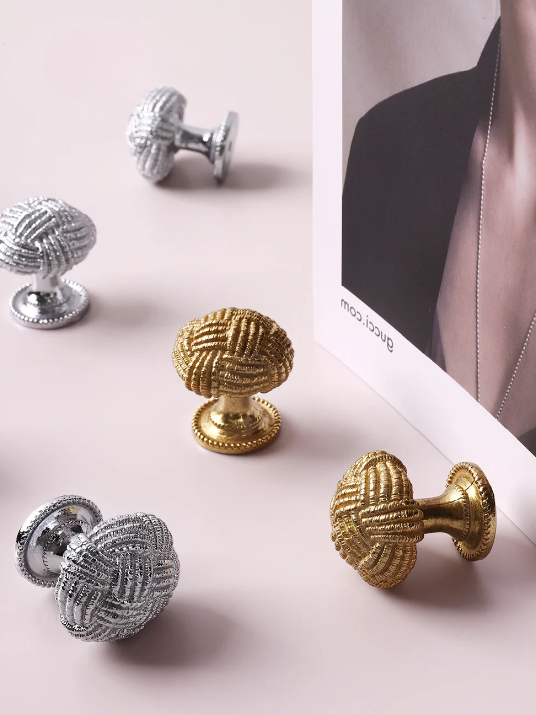 Decorative cabinet knobs in gold and silver on a light pink surface.