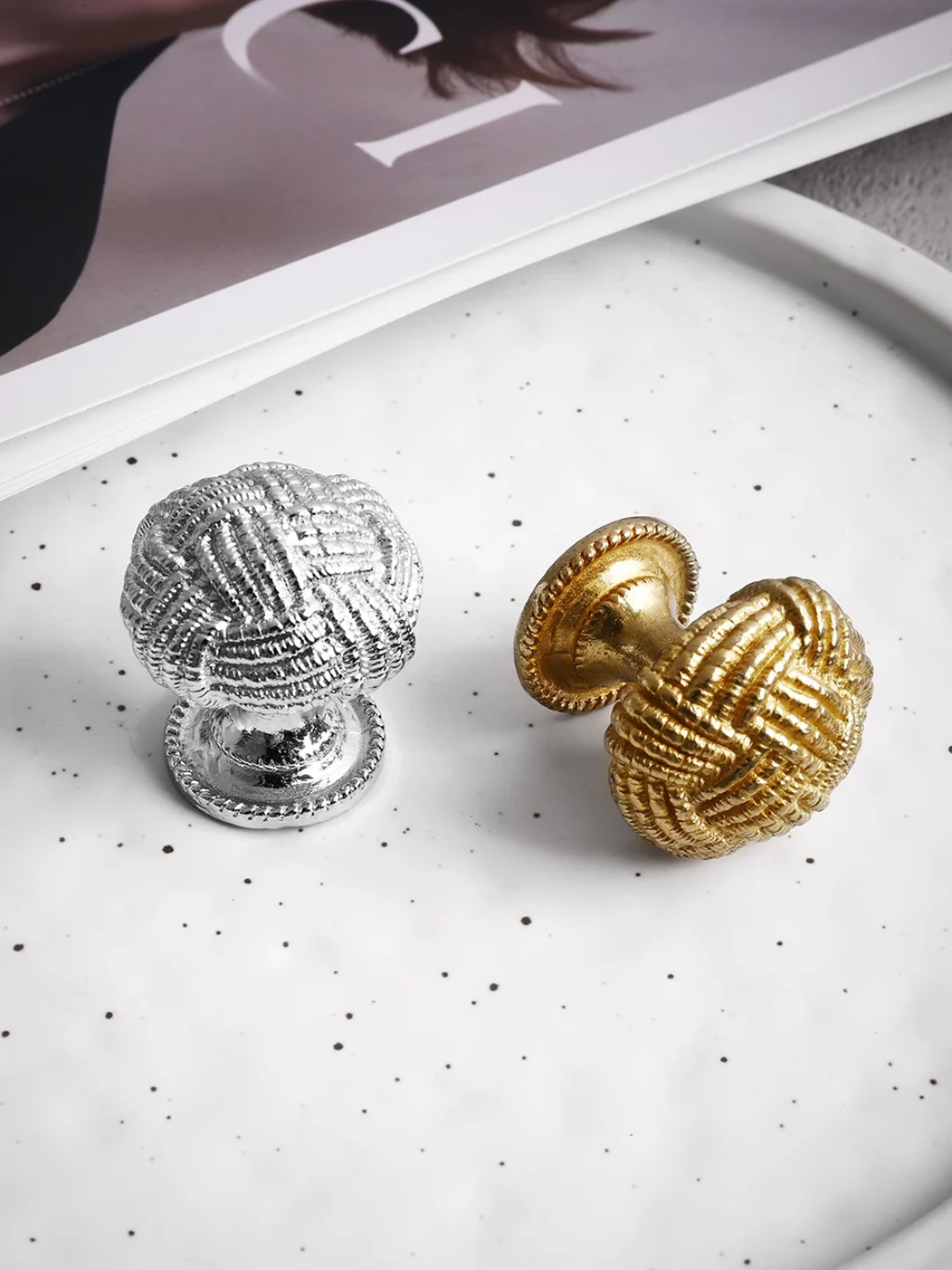 Silver and gold cabinet knobs on a white surface with a magazine in the background