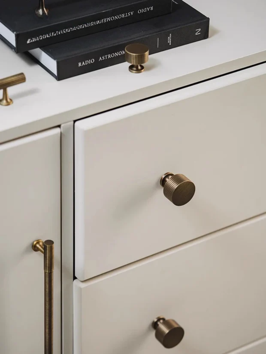 Close-up of a light-colored cabinet with brass knobs and books on top.