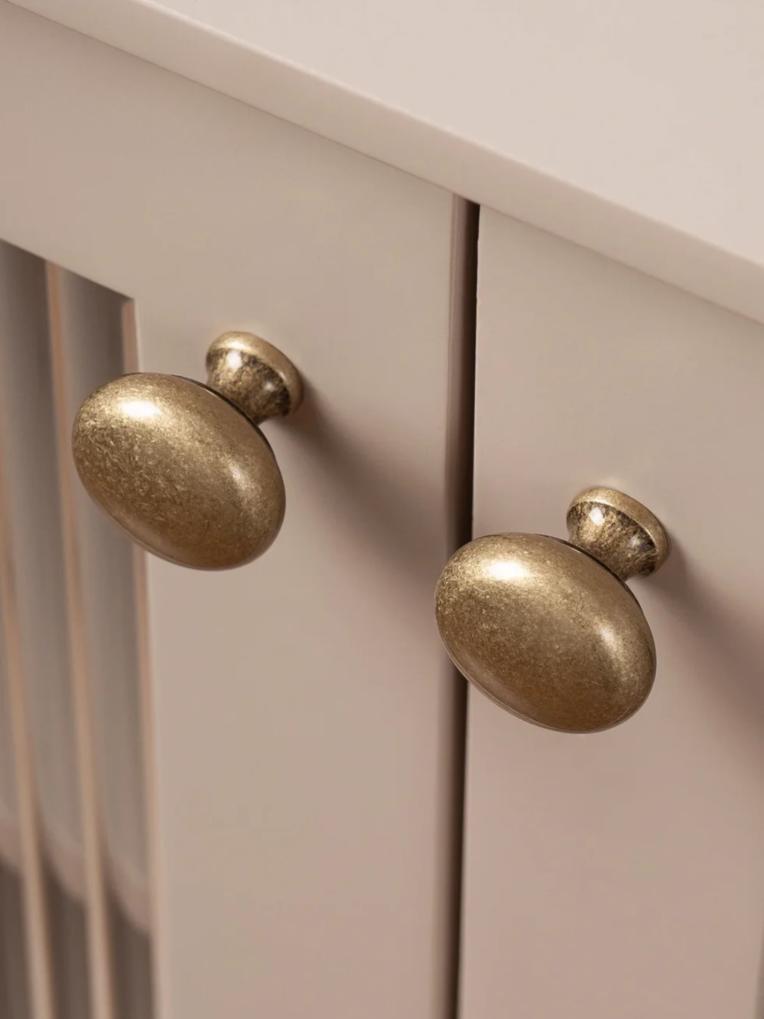 Close-up of two gold cabinet knobs on a white cabinet.