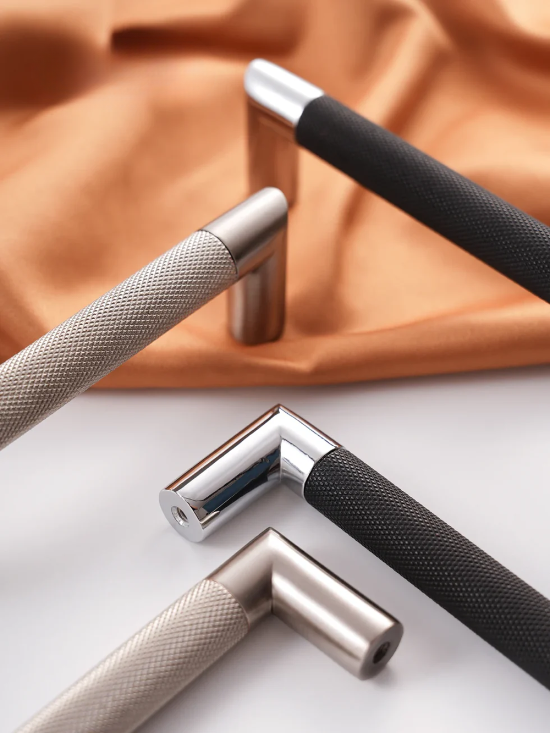 Three metallic door handles on a white surface with an orange fabric background