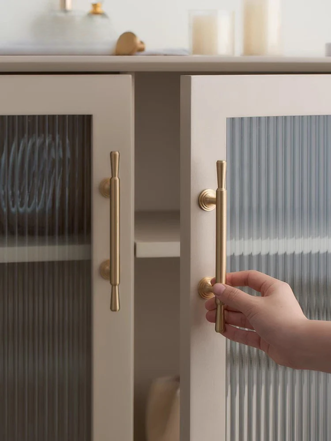 Hand opening a cabinet door with gold handles in a kitchen setting