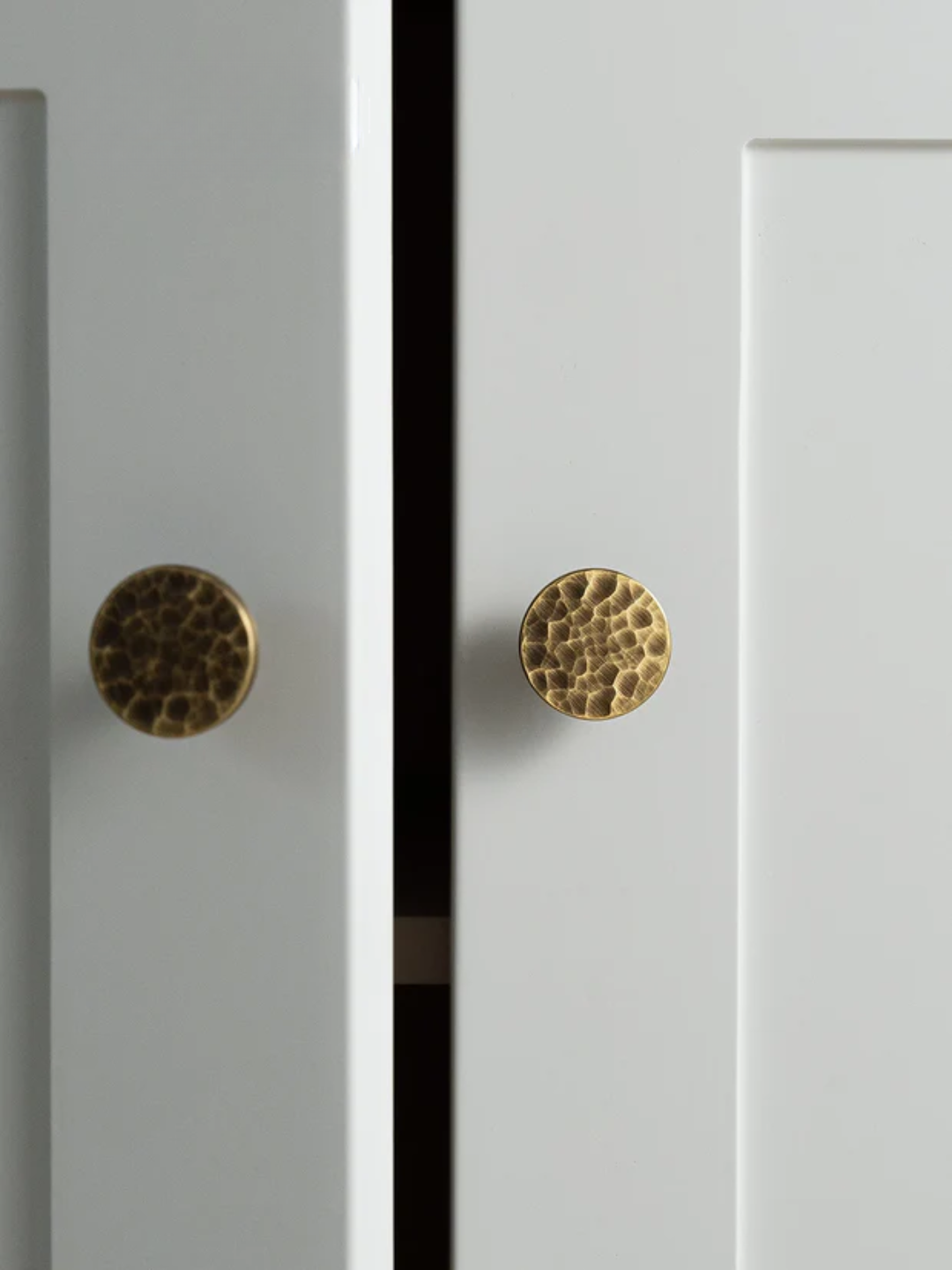 Close-up of two white cabinet doors with gold textured knobs.
