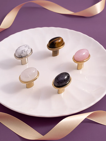 Decorative cabinet knobs with marble and gemstone finishes on a white plate with gold ribbons.