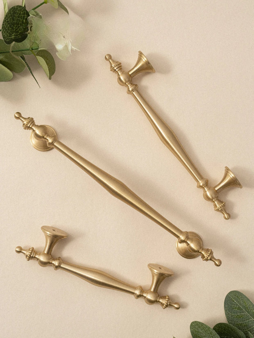 Set of gold door handles on a beige background with greenery