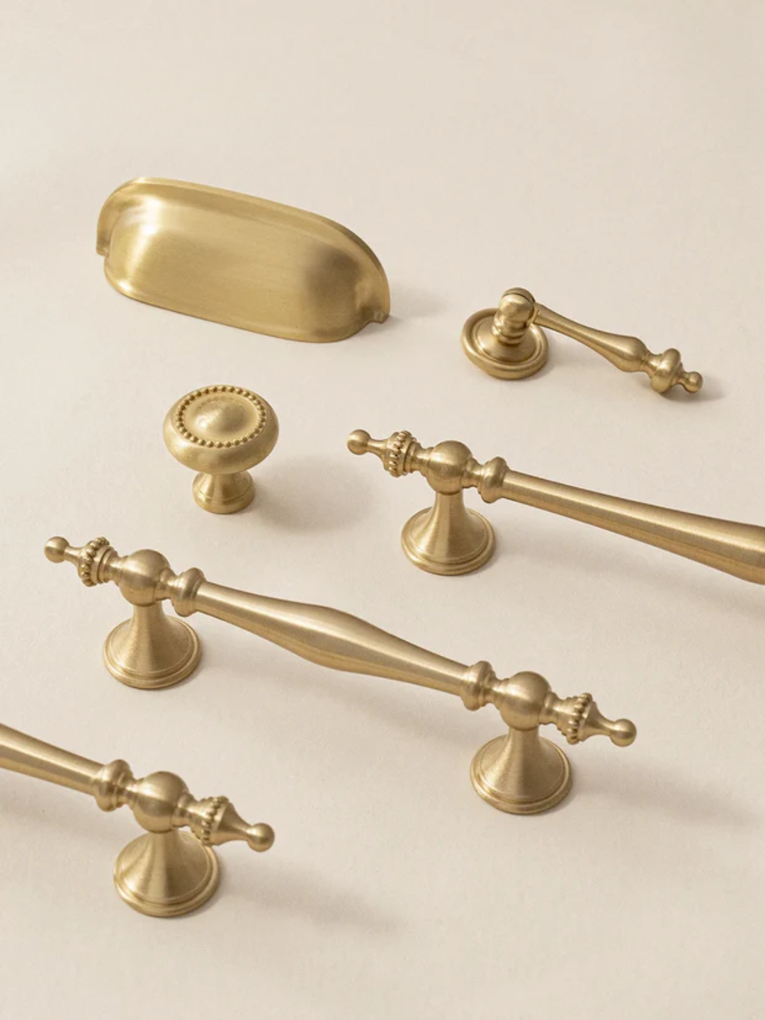Collection of gold cabinet handles and knobs on a beige background
