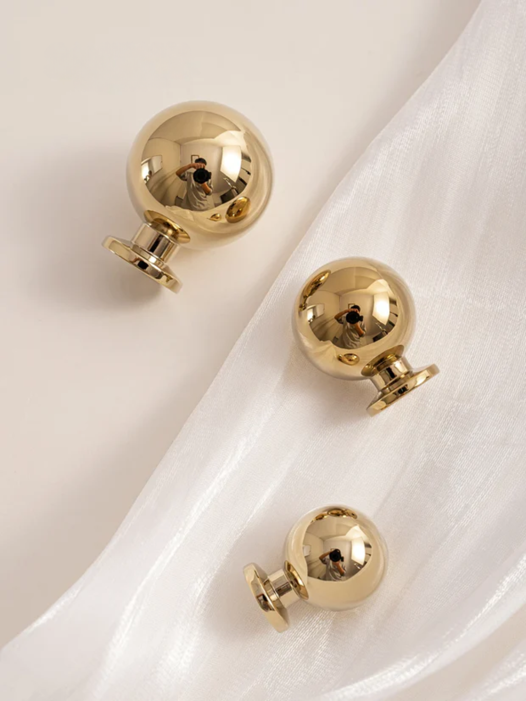 Gold spherical earrings on a white fabric background.