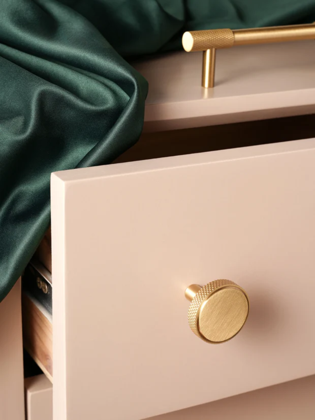 Close-up of a pink drawer with gold knobs and green fabric in the background