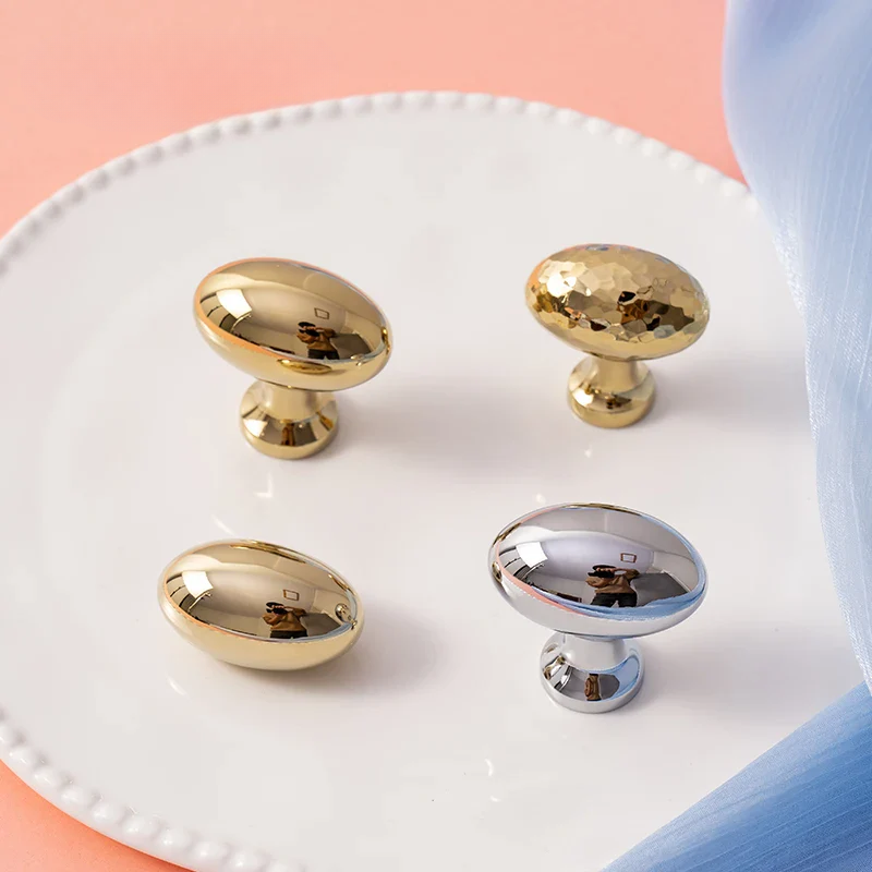 Gold and silver cabinet knobs on a white plate with a pink background