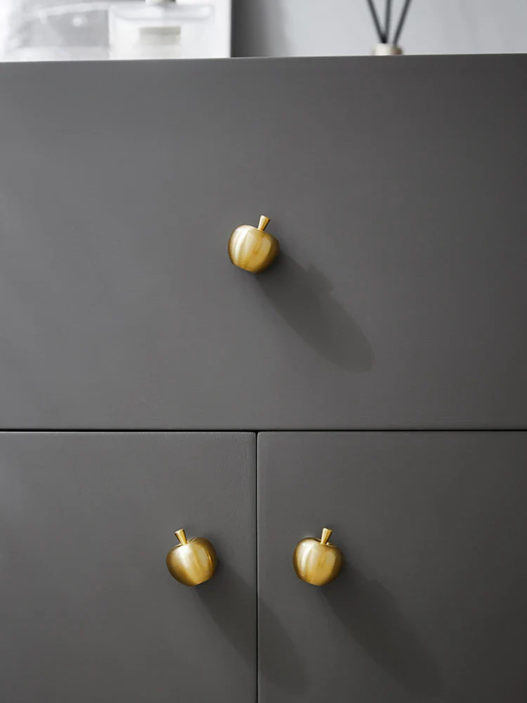 Dark gray cabinet with gold apple-shaped knobs on a neutral background