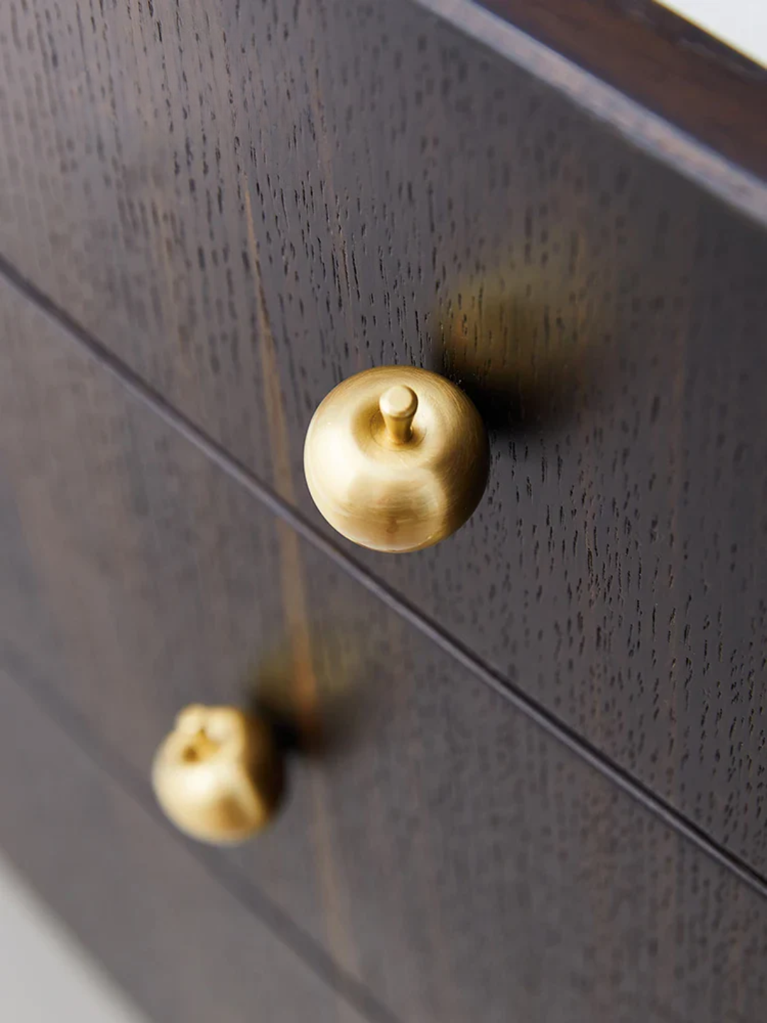 Close-up of a dark wooden drawer with gold knobs.