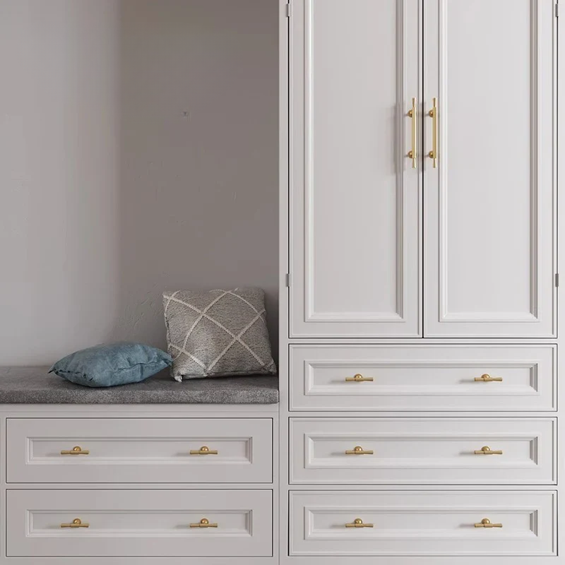 Gray wardrobe with gold handles and a gray cushion on a bench against a white wall.