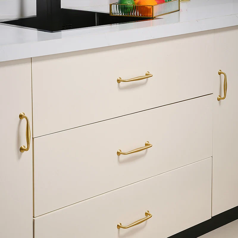 Close-up of a kitchen cabinet with gold handles on a white countertop.