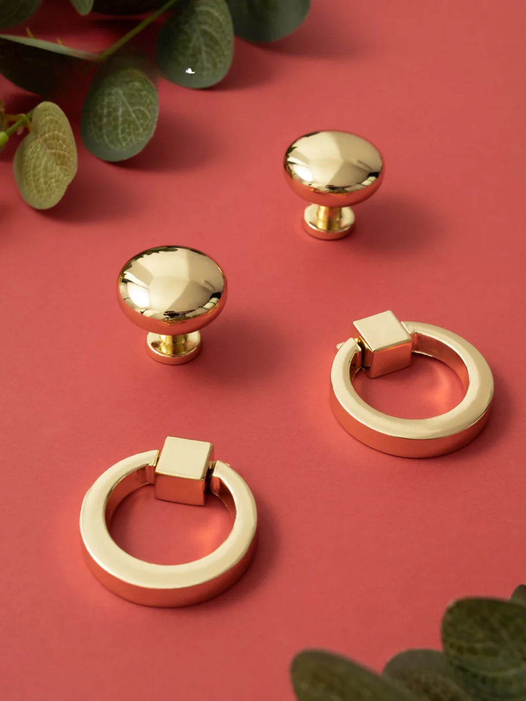 Gold cabinet knobs on a red background with green leaves.