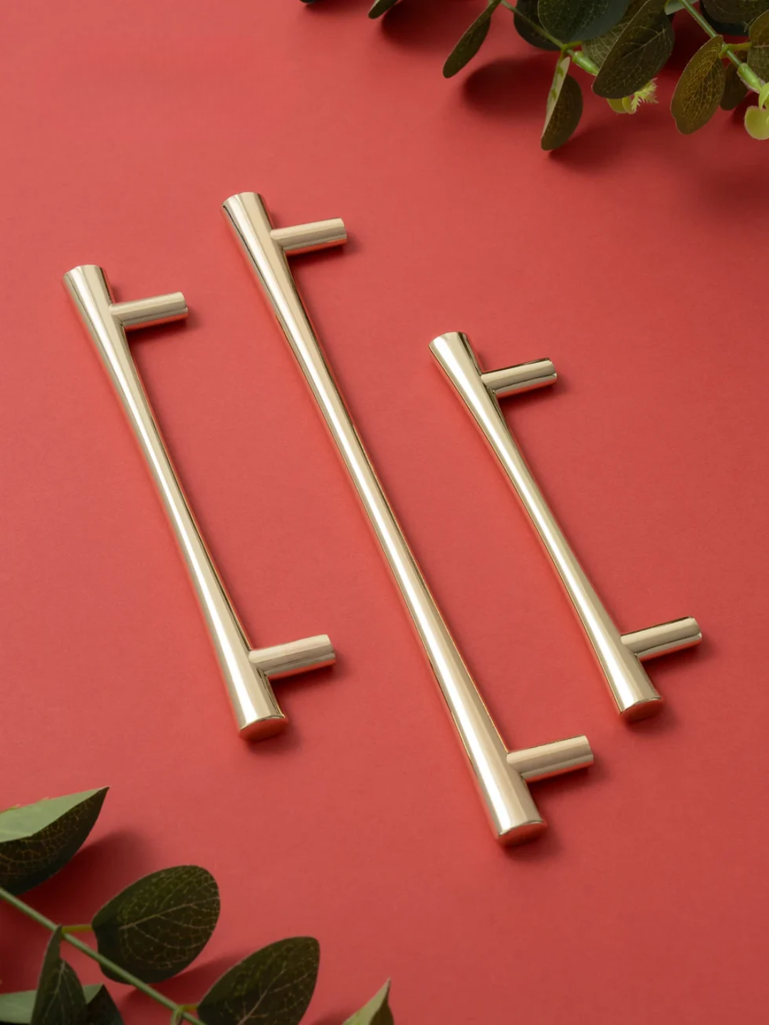 Three gold cabinet handles on a red background with green leaves.